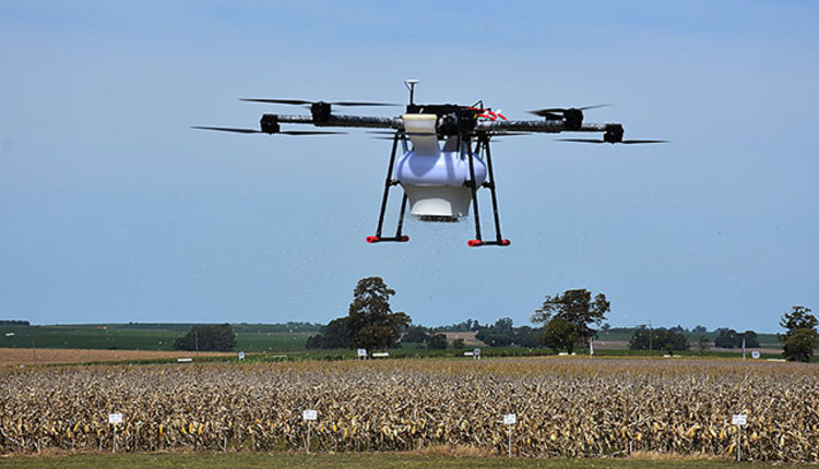 A drone in a field, flying and dropping off seed pods.